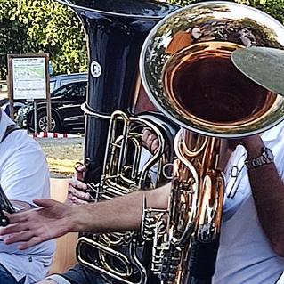 Musiker spielen verschiedene Blechblasinstrumente, während ein Warnschild für spielende Kinder im Hintergrund sichtbar ist.