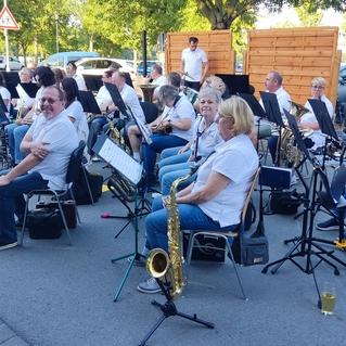 Musikgruppe in weißen T-Shirts spielt im Freien, umgeben von Stühlen und Notenständern.