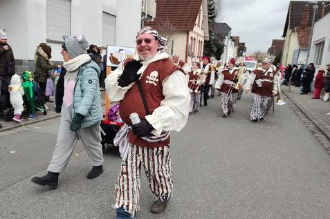 Karnevalsumzug mit verkleideten Menschen, darunter ein Pirat, der fr&ouml;hlich auf der Stra&szlig;e posiert.