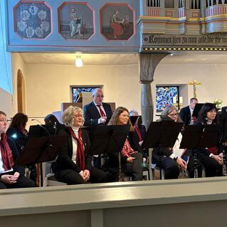 Chorgruppe mit Notenständern in einer Kirche, Musikerinnen und Musiker warten auf ihren Auftritt.