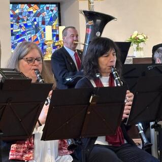Musikgruppe mit Klarinettenspielern in einer Kirche, im Hintergrund ein Posaunist und ein buntes Fenster.