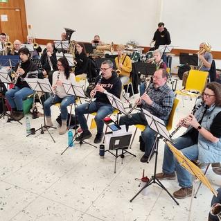 Proben eines Orchesters mit Instrumentalisten, die Notenblätter vor sich haben, in einem hellen Raum.