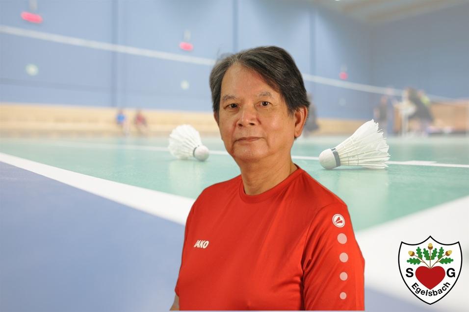 Porträt einer Sportlerin in roter Sportkleidung vor einem Badmintonfeld mit Federbällen im Hintergrund.