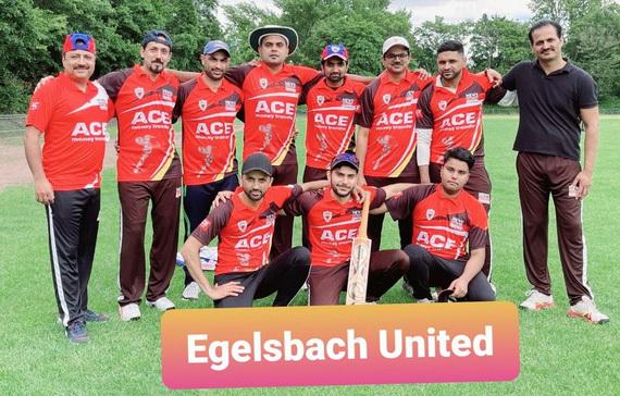 Gruppenfoto der Cricketmannschaft Egelsbach United in roten Trikots auf einem gr&uuml;nen Sportplatz.
