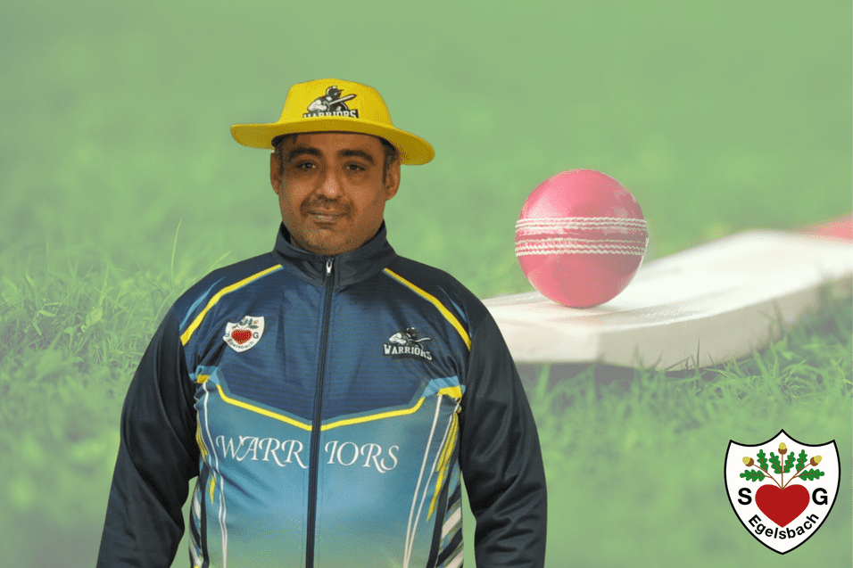 Mann in gelbem Hut und Sportjacke steht vor einem pinken Cricketball und Schläger auf grünem Rasen.