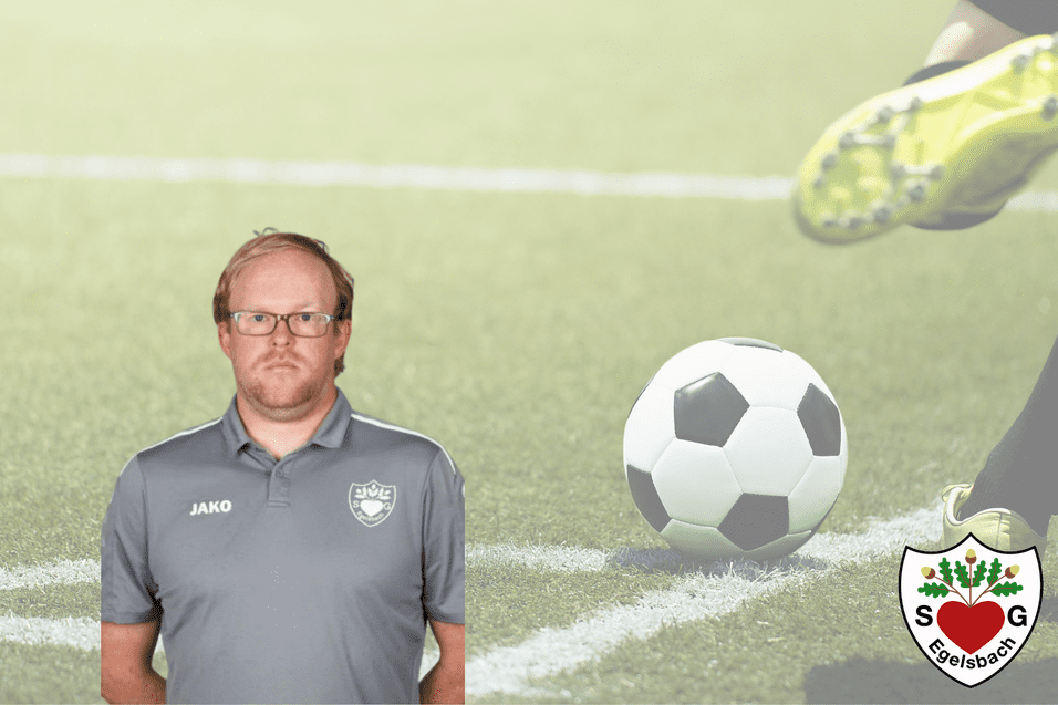 Mann mit Brille steht auf einem grünen Fußballplatz, im Hintergrund ein rollender Fußball und ein Spieler in Aktion.