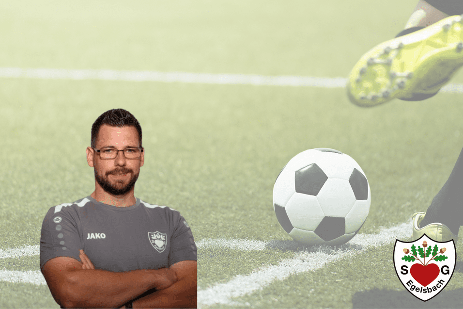 Trainer im grauen Sporttrikot steht auf einem Fußballfeld mit einem Ball und einem Spieler, der zum Schuss ansetzt.
