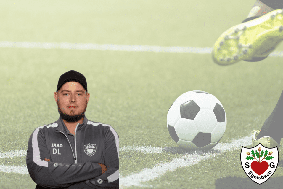 Mann in Sportjacke posiert vor einem Fußball, der auf einem Rasenplatz gespielt wird, mit Vereinsemblem im Hintergrund.