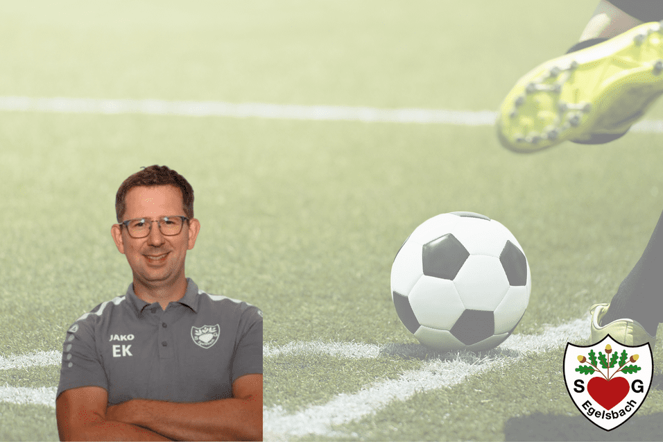 Trainer steht lächelnd im Vordergrund, mit einem Fußball im Hintergrund auf einem Sportplatz.