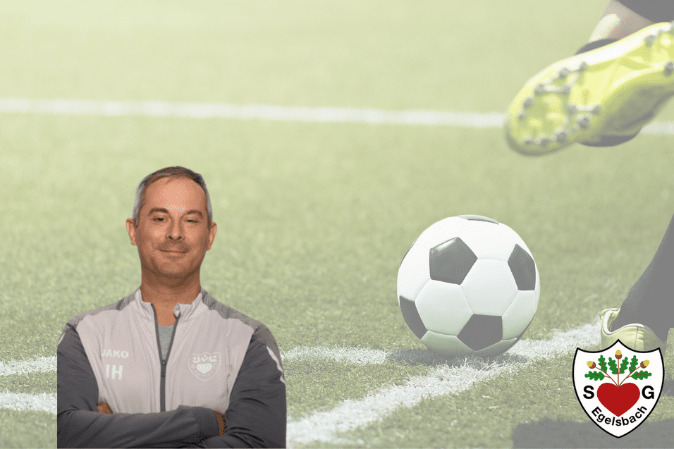 Trainer steht lächelnd auf einem Fußballfeld, während ein Ball im Vordergrund zu sehen ist.