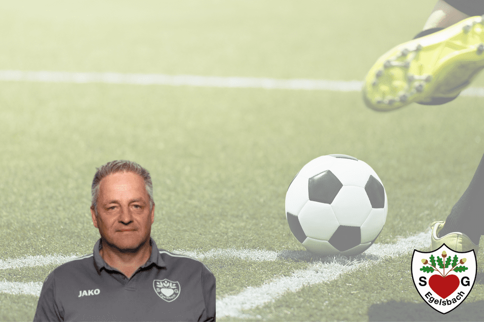 Trainer mit grauem Polohemd steht vor einem sich bewegenden Fußball auf einem Rasenplatz im Hintergrund.