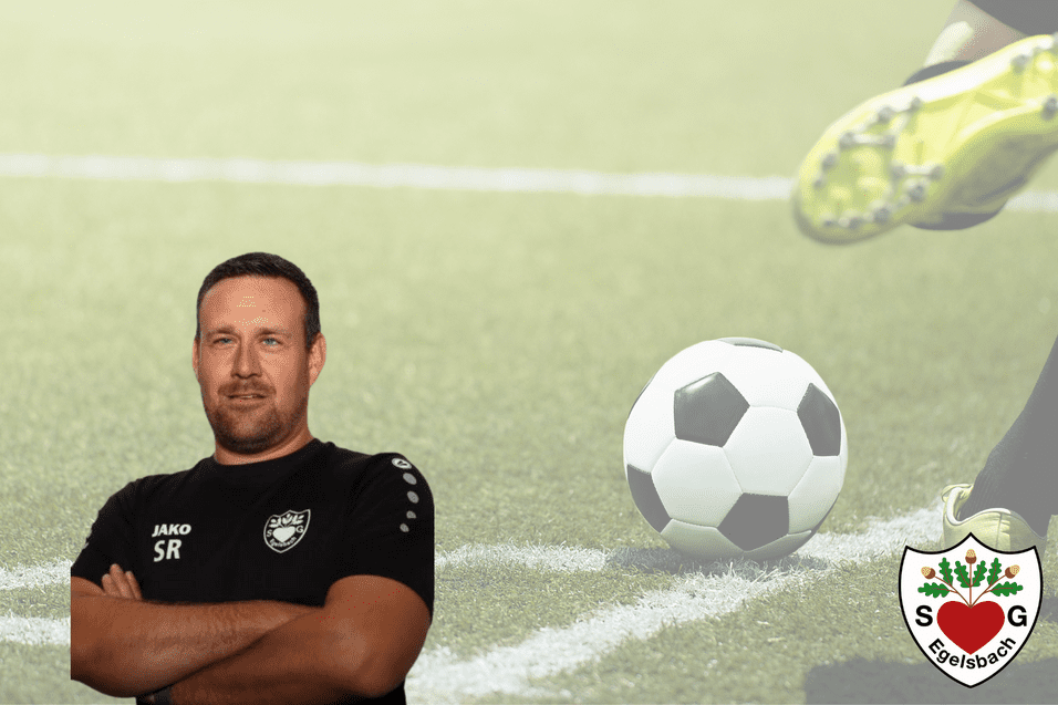 Trainer im Sportanzug mit verschränkten Armen auf einem Fußballplatz, im Hintergrund ein rollender Fußball.