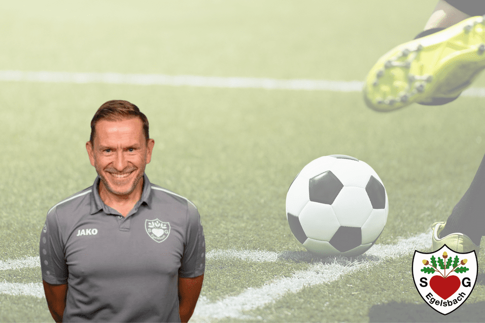 Ein lächelnder Mann mit Kurzhaarschnitt in grauem Poloshirt steht vor einem Fußballfeld und einem Ball.