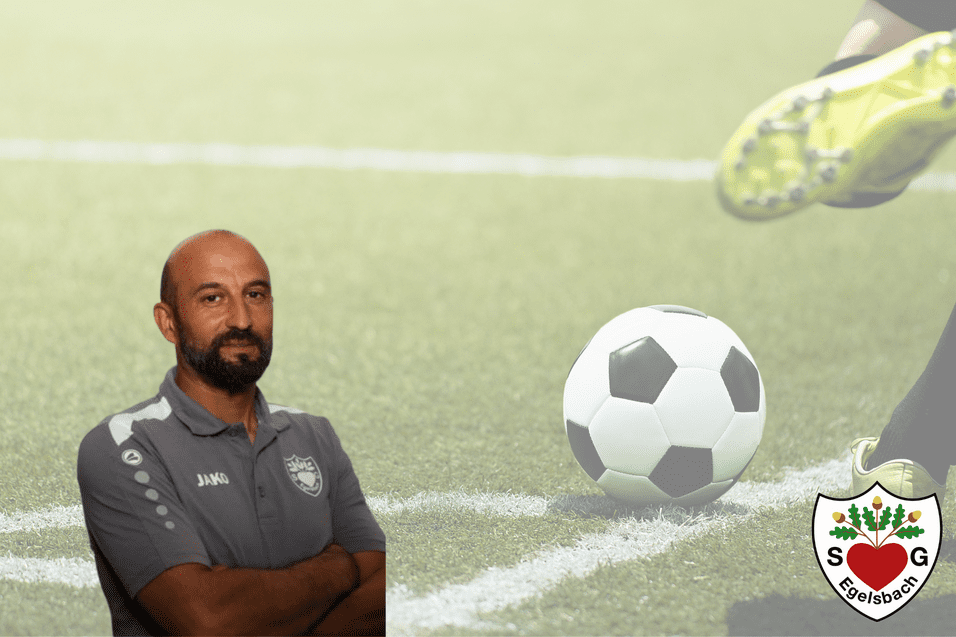 Mann im Trainerstall mit kurzem Bart, neben einem Fußball auf einem grasbewachsenen Spielfeld.