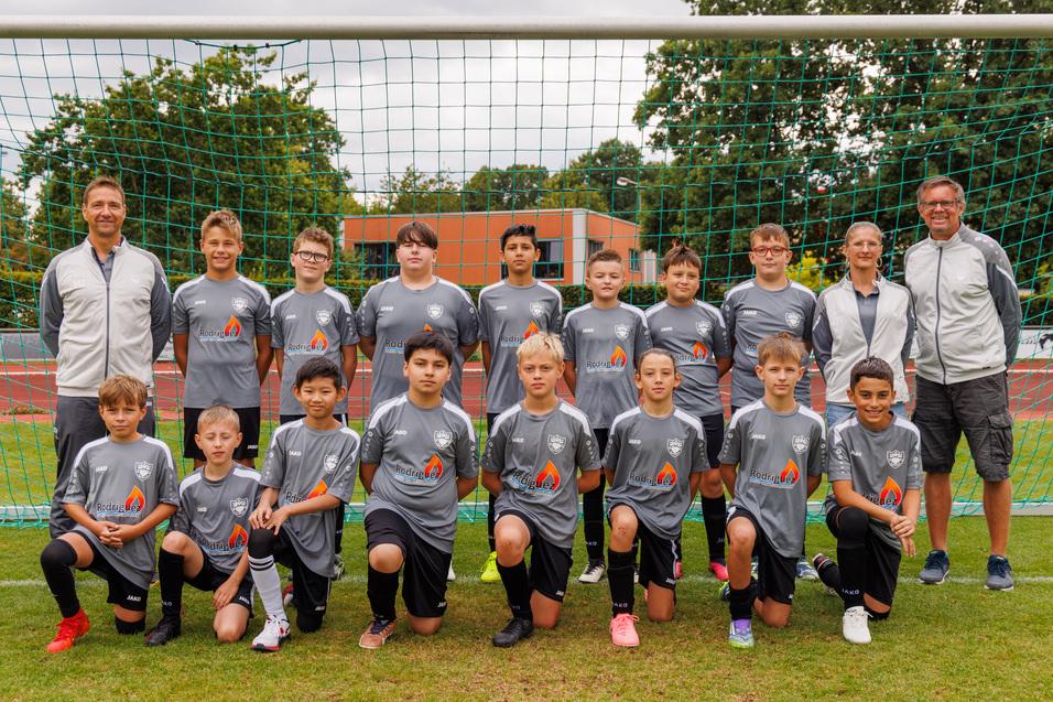 Grupppenfoto einer Fu&szlig;ballmannschaft mit 14 Spielern in grauen Trikots und zwei Trainern vor einem Tornetz.