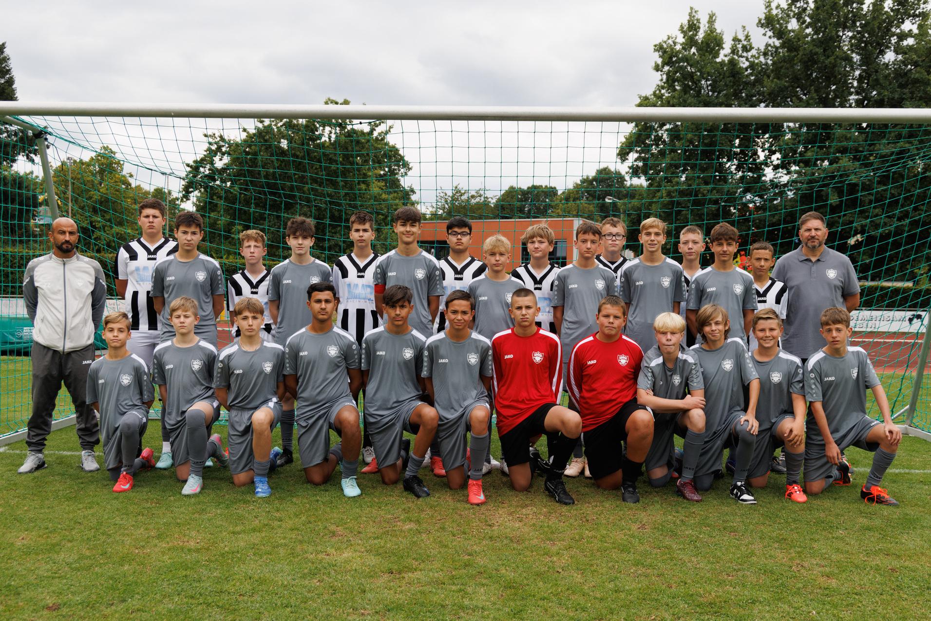 Gruppenaufnahme einer Fußballmannschaft von Jugendlichen in grauen und schwarz-weißen Trikots vor einem Tor.
