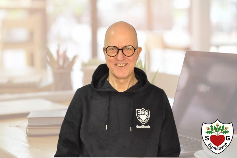 Mann mit Brille und Glatze in schwarzem Hoodie sitzt vor einem Laptop und Pflanzen auf einem Tisch.