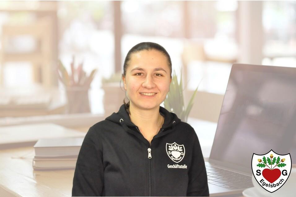 Portr&auml;t einer l&auml;chelnden Frau in schwarzer Jacke vor einem Laptop und Pflanzen im Hintergrund.