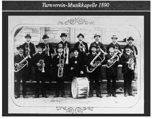 Gruppenfoto der Turnverein-Musikkapelle von 1890 mit Musikern in historischen Kleidern und Instrumenten, einschlie&szlig;lich einer Trommel.