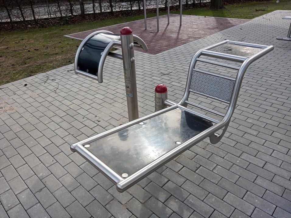 Fitnessger&auml;t im Freien: Metallische Liege mit Griffen auf einem gepflasterten Boden.