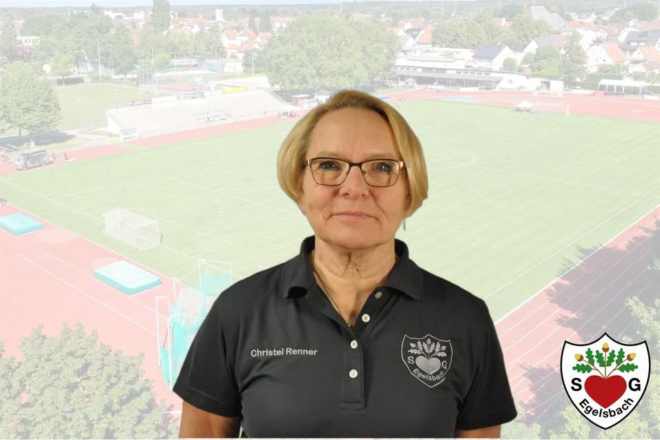 Frau mit Brille steht vor einem Sportplatz, im Hintergrund sind eine Laufbahn und ein Fu&szlig;ballfeld zu sehen.