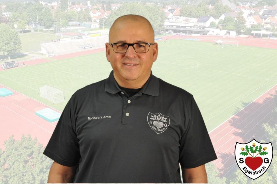 Portr&auml;t eines Mannes mit Brille in Schwarz, vor einem Sportplatz mit Fu&szlig;ballfeld im Hintergrund.