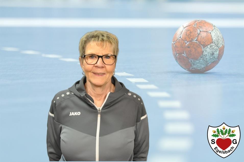 Porträt einer lächelnden Frau in sportlicher Kleidung vor einem Handballfeld mit einem Handball im Hintergrund.
