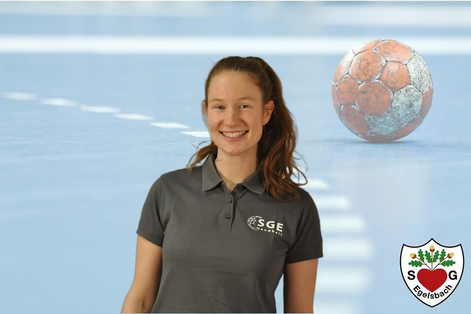 L&auml;chelnde Frau in einem grauen Polo-Shirt vor verschwommenem Handball und Sportfl&auml;che. Logo in der Ecke.