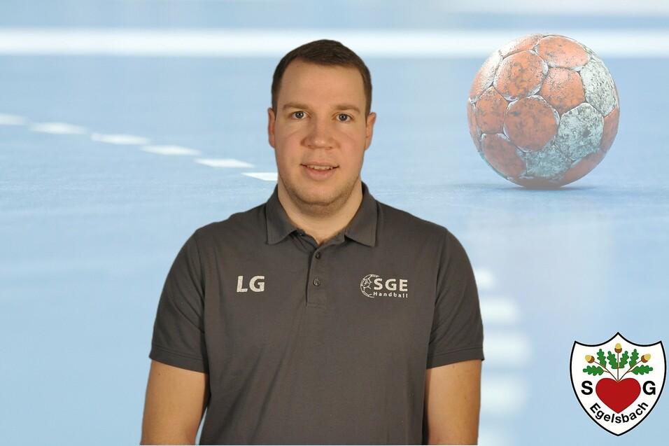Portrait eines Mannes in grauem Poloshirt mit Logo, Hintergrund zeigt einen Handball und eine Sporthalle.