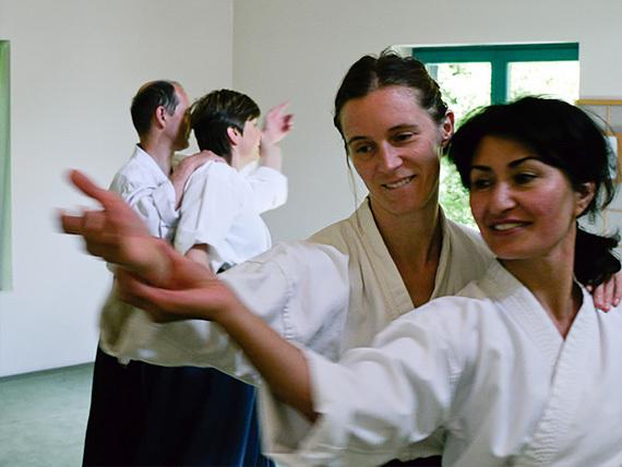 Vier Personen in Aikido-Training stehen in einer geschlossenen Gruppe und &uuml;ben Bewegungen in einem hellen Raum.