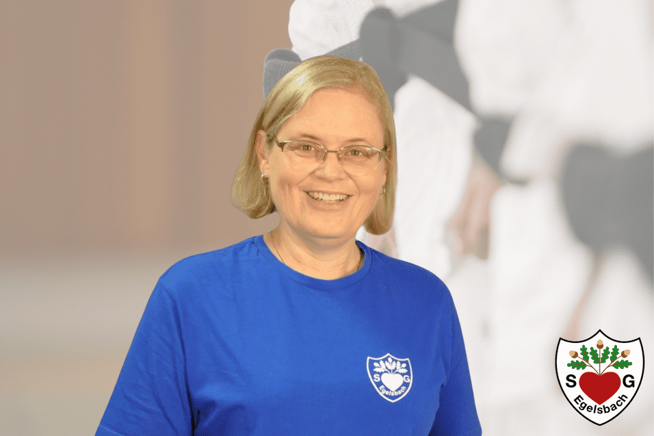 Lächelnde Frau in blauer T-Shirt vor verschwommenem Hintergrund, Logo in der Ecke.