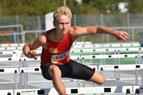 Junger L&auml;ufer &uuml;berquert eine H&uuml;rde auf einer Sportanlage w&auml;hrend eines Wettkampfs.