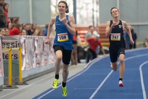 Zwei Athleten sprinten auf einer blauen Laufbahn in einer Halle, Nummern auf den Trikots: 159 und 747.