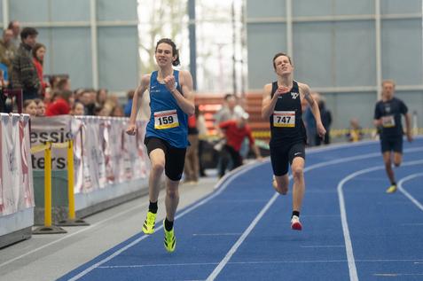 Zwei Athleten sprinten auf einer blauen Laufbahn in einer Halle, Nummern auf den Trikots: 159 und 747.