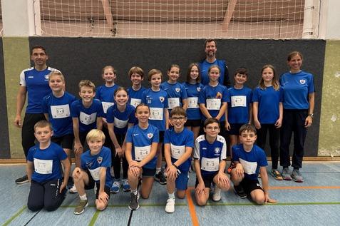 Gruppenfoto von 17 Kindern in blauen Sportshirts und Trainern in einer Turnhalle, alle l&auml;cheln in die Kamera.