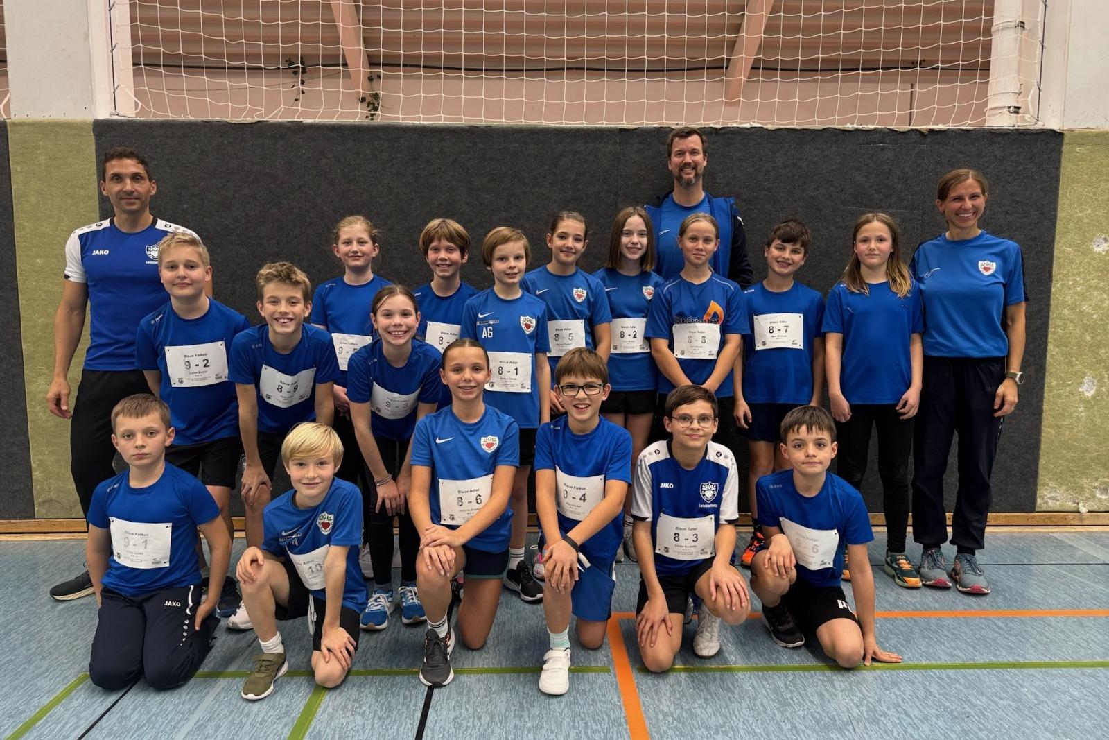 Gruppenfoto von 17 Kindern in blauen Sportshirts und Trainern in einer Turnhalle, alle l&auml;cheln in die Kamera.