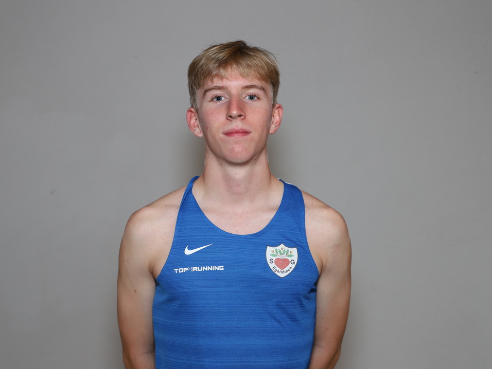 Junger Mann mit blonden Haaren tr&auml;gt ein blaues Sportshirt und steht vor einem neutralen Hintergrund.