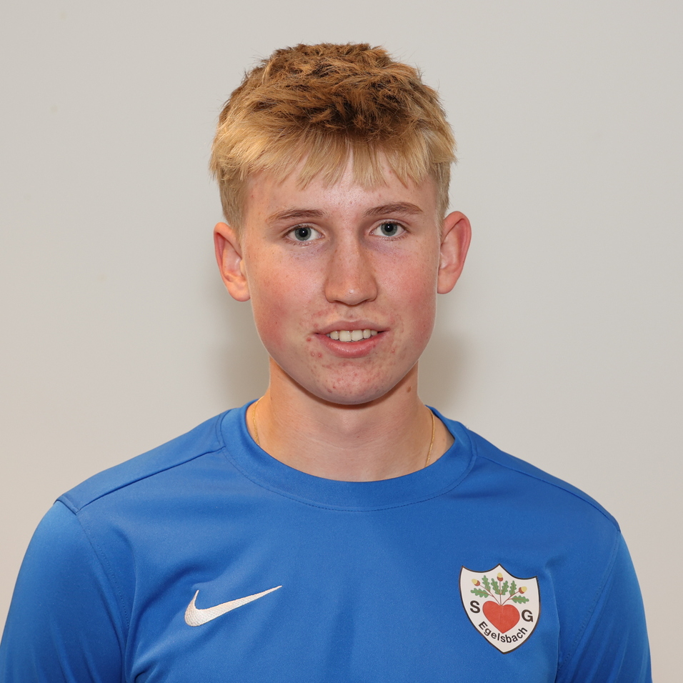 Junger Mann mit blondem Haar in blauer Sportjacke, l&auml;chelt vor grauem Hintergrund.