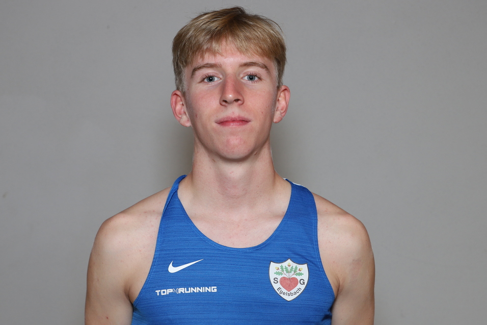 Junger Mann mit blonden Haaren tr&auml;gt ein blaues Sportshirt und steht vor einem neutralen Hintergrund.