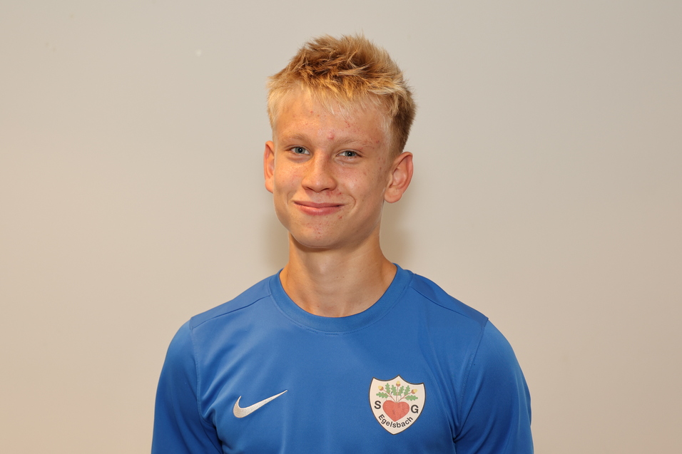 Junger Mann mit blonden Haaren in blauer Sportbekleidung, l&auml;chelt vor neutralem Hintergrund.