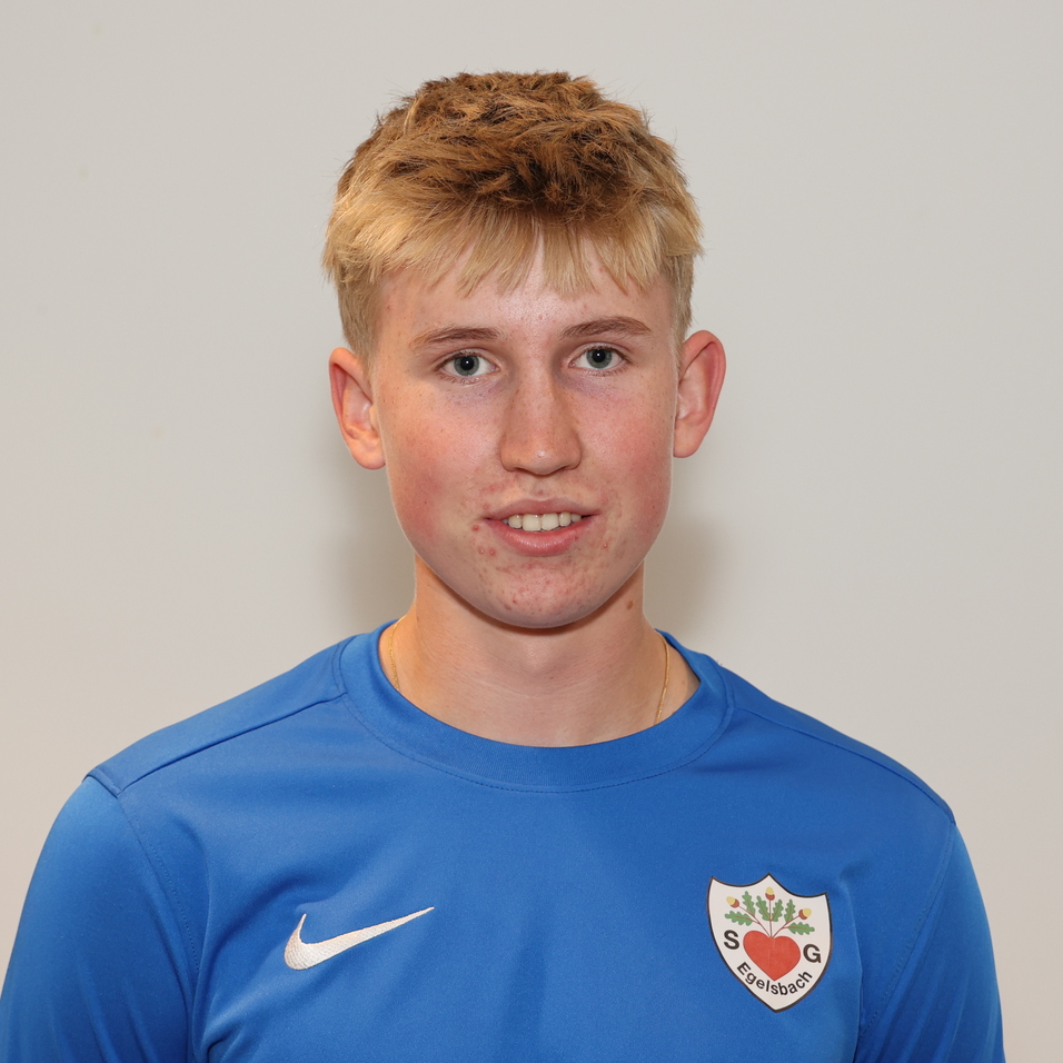 Junger Mann mit blondem Haar in blauer Sportjacke, l&auml;chelt vor grauem Hintergrund.