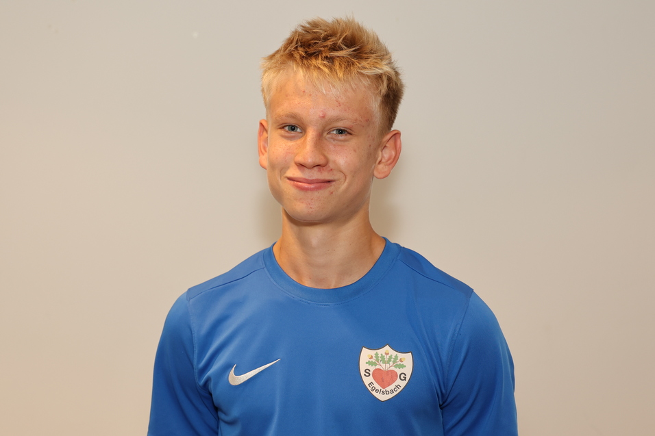 Junger Mann mit blonden Haaren in blauer Sportbekleidung, l&auml;chelt vor neutralem Hintergrund.