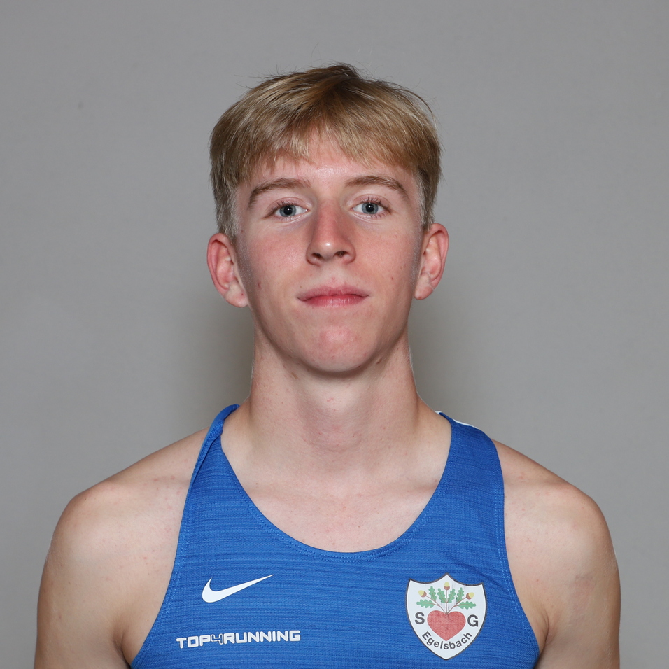 Junger Mann mit blonden Haaren tr&auml;gt ein blaues Sportshirt und steht vor einem neutralen Hintergrund.