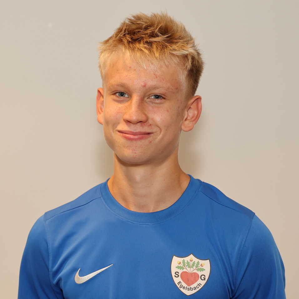 Junger Mann mit blonden Haaren in blauer Sportbekleidung, l&auml;chelt vor neutralem Hintergrund.