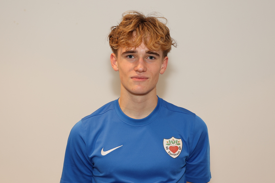 Junger Mann mit lockigem, blondem Haar in blauem Sporttrikot vor einem hellen Hintergrund.