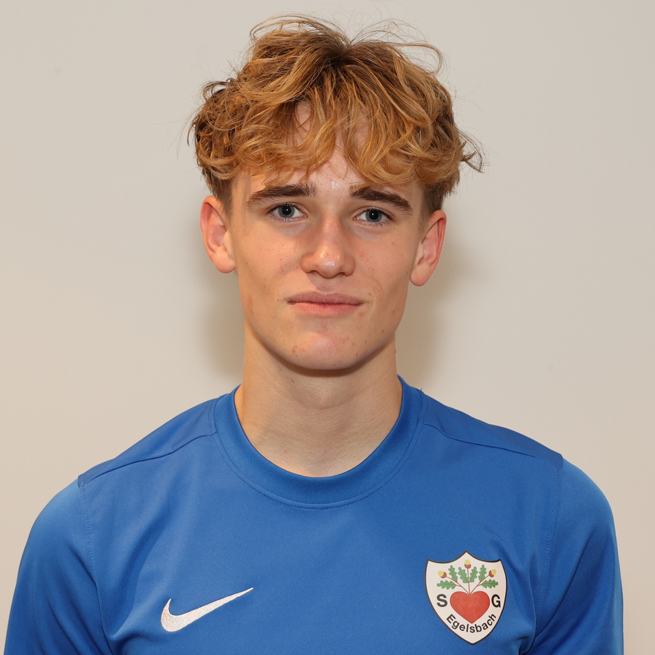 Junger Mann mit lockigem, blondem Haar in blauem Sporttrikot vor einem hellen Hintergrund.