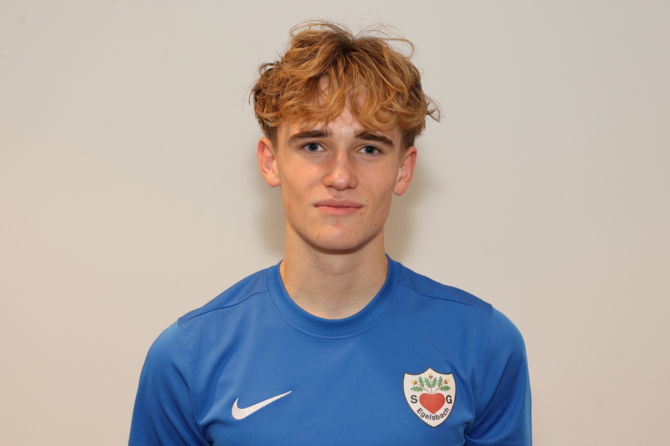 Junger Mann mit lockigem, blondem Haar in blauem Sporttrikot vor einem hellen Hintergrund.