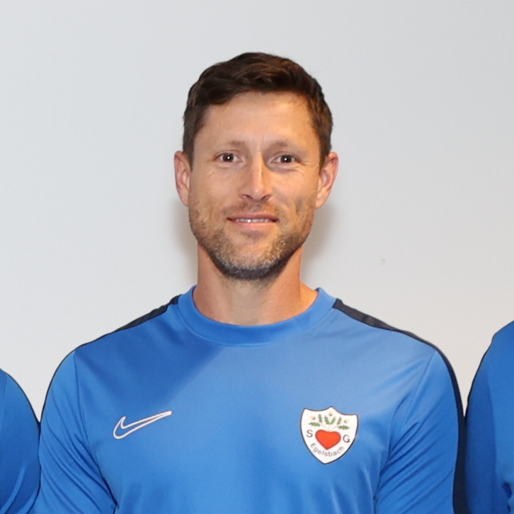 Gruppe von zw&ouml;lf Personen in blauen T-Shirts, die in zwei Reihen auf einem Fliesenboden stehen.
