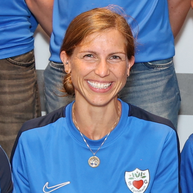 Gruppe von zw&ouml;lf Personen in blauen T-Shirts, die in zwei Reihen auf einem Fliesenboden stehen.