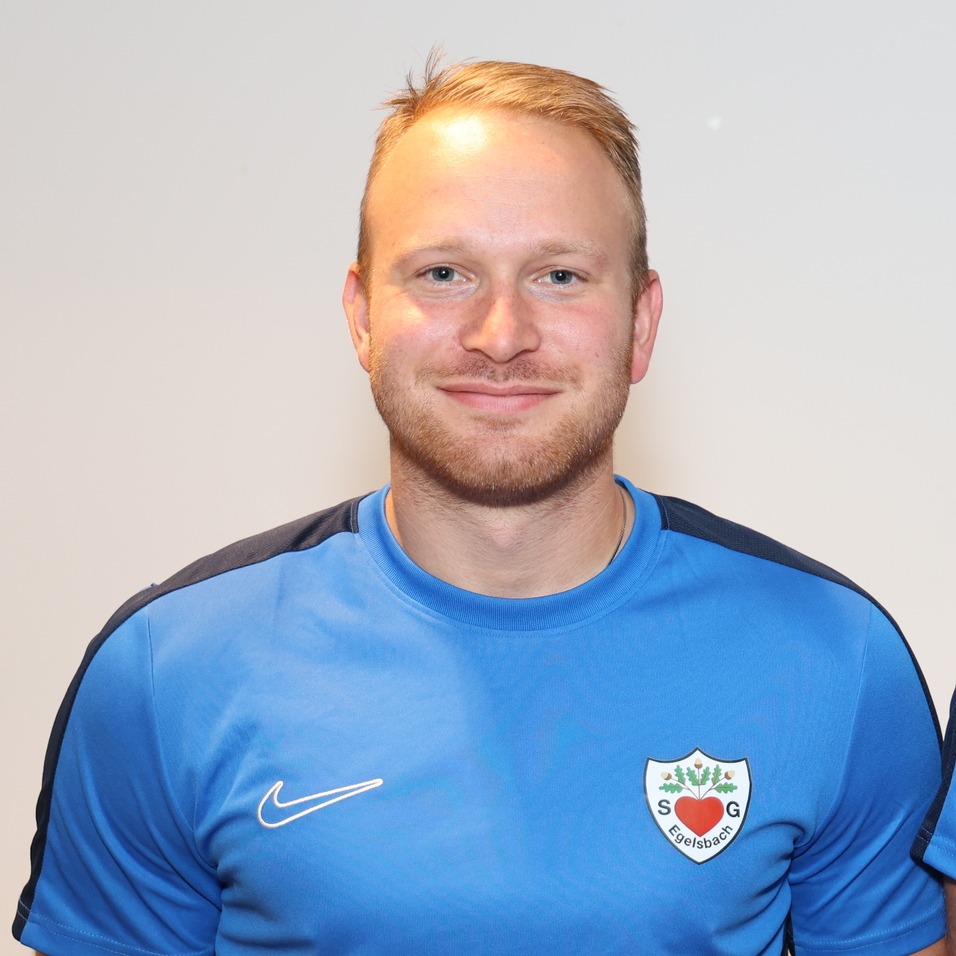 Portr&auml;t von zwei M&auml;nnern in blauen Sporttrikots, l&auml;chelnd, nebeneinander vor neutralem Hintergrund.